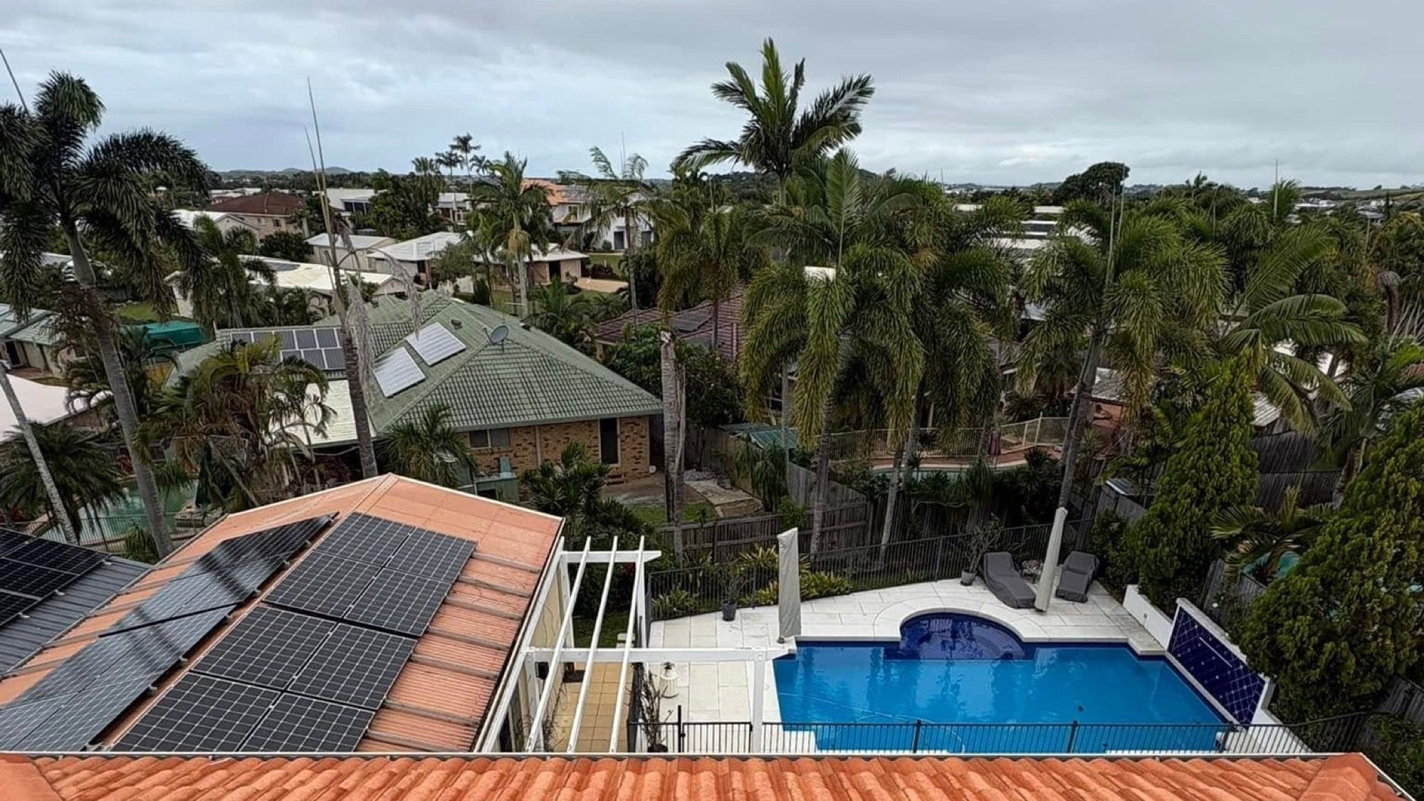 A terracotta tiled roof with solar panels above a backyard pool in Mackay