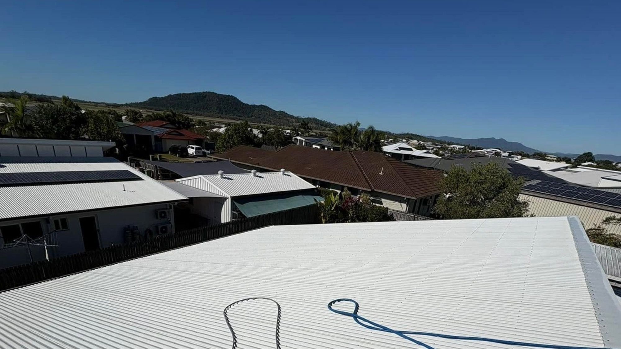 A wide metal roof with a hose running across it and hills in the distance