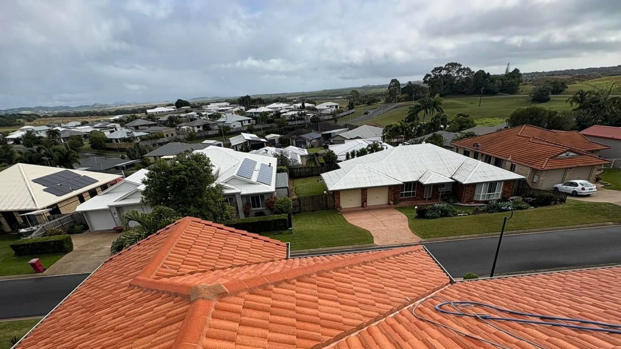 Terracotta tiled roofs across a Mackay street with a cleaning hose laid over one of them