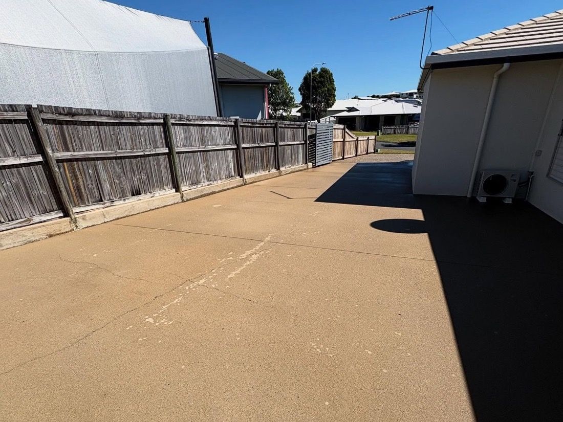 A concrete path running between a house wall and a fence