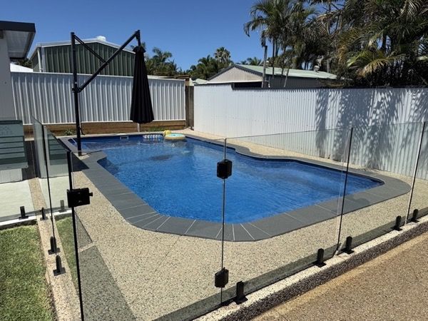 A backyard pool with a glass fence and exposed aggregate surround