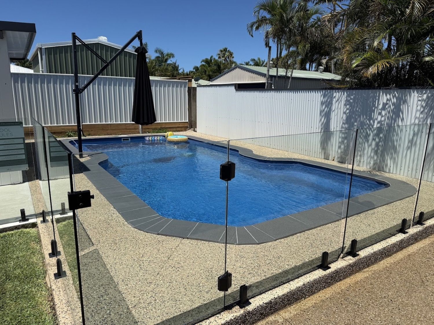 A backyard pool with a glass fence and exposed aggregate surround